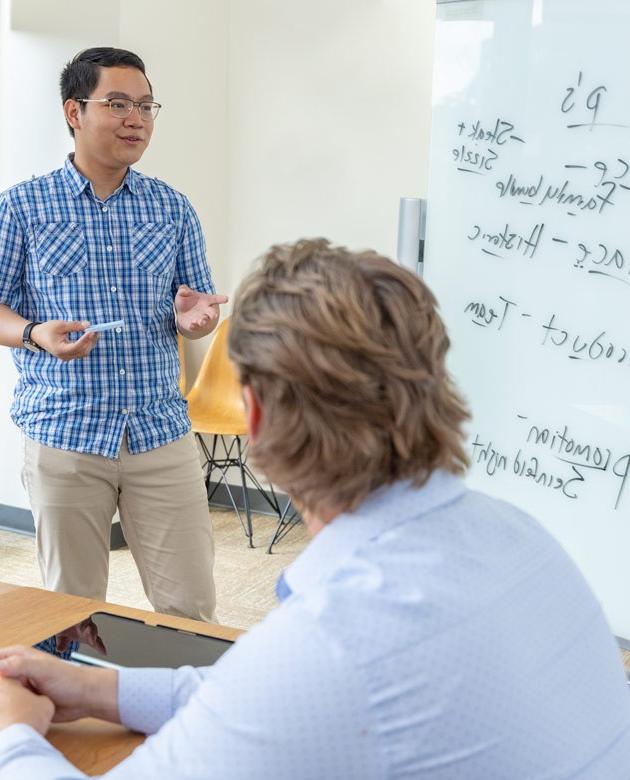 Two U N E students review the "4 P's" on a whiteboard